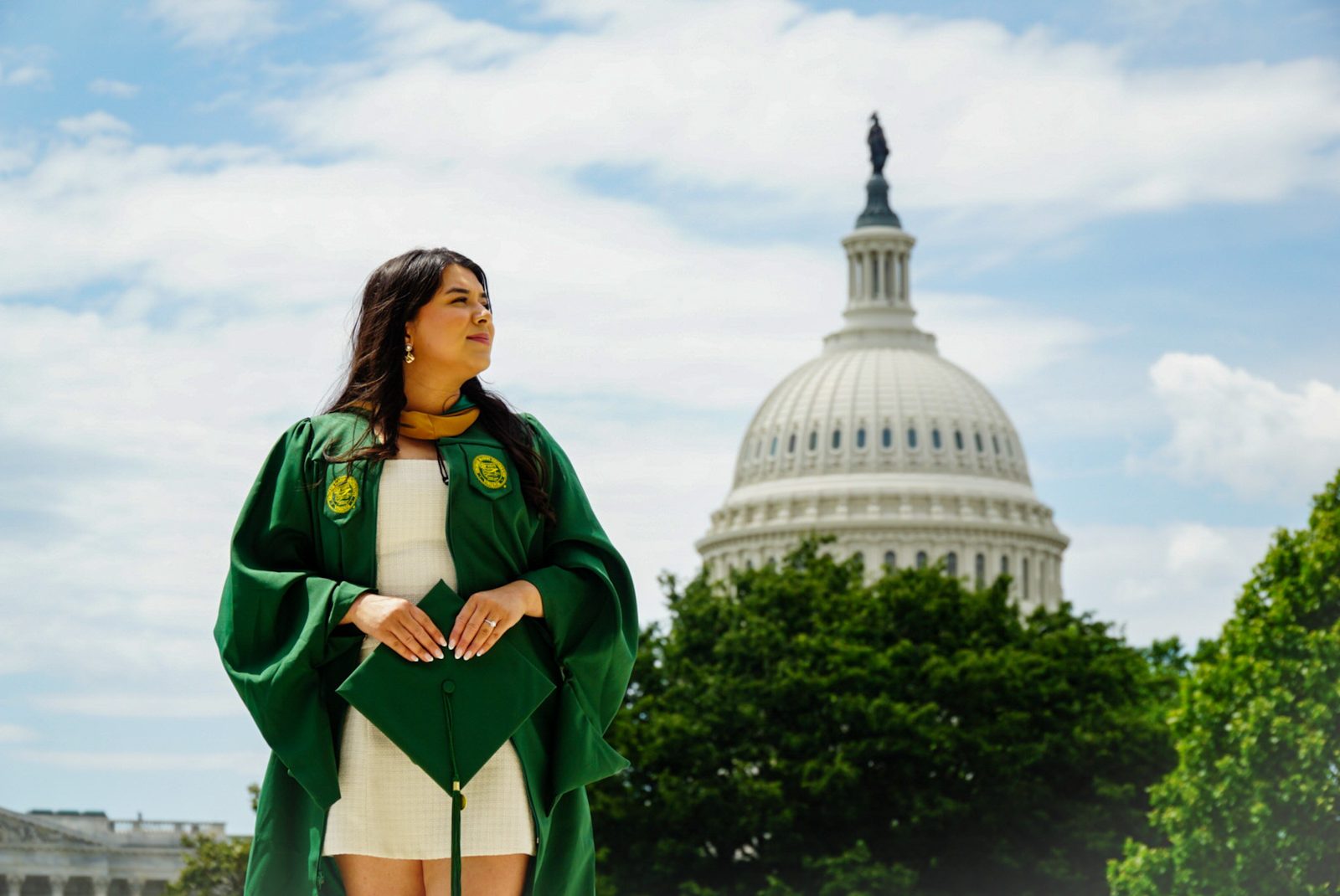 Graduate in a green cap and gown in front of the U.S. Capitol dome